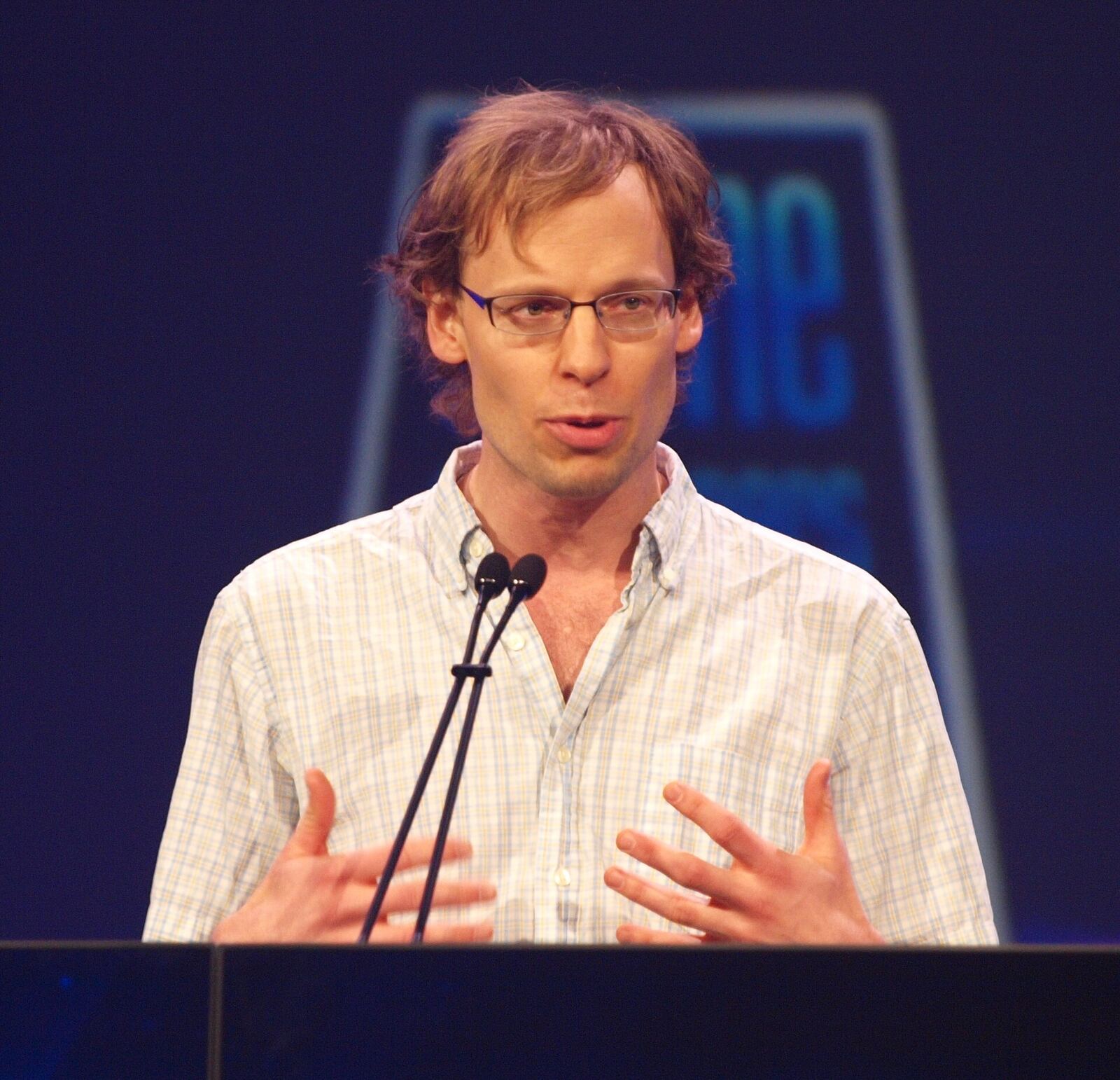 Chris Hecker speaks at a podium during a presentation at the Game Developers Conference, showcasing graphics expertise.