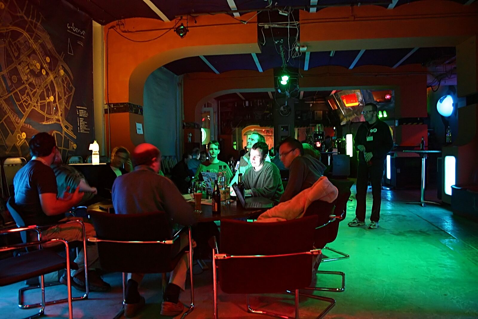 People socialize at tables during the Wikimedia Conference Berlin, discussing MediaWiki development and digital culture.